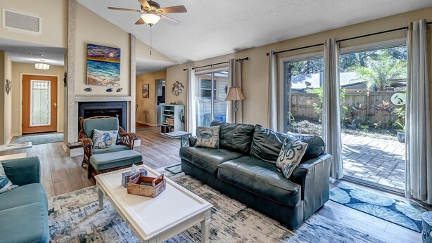 A spacious living room with a fireplace, a ceiling fan, and a large sliding glass door leading to a backyard. - Coastal Oaks - Atlantic Beach home just 3 blocks from the beach (Atlantic Beach)
