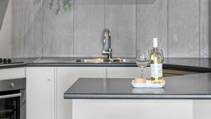Una cocina de diseño moderno, con un lavamanos de acero inoxidable, una botella de vino y una copa de vino sobre una encimera blanca.