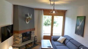 Ein Wohnzimmer mit Kamin aus Stein, einem großen Flachbildfernseher, einer Couch und einer Deckenleuchte.