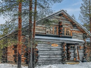 Eine Blockhütte mit freundlichem Schild, mehreren Fenstern und einem mit Schnee bedeckten Dach.