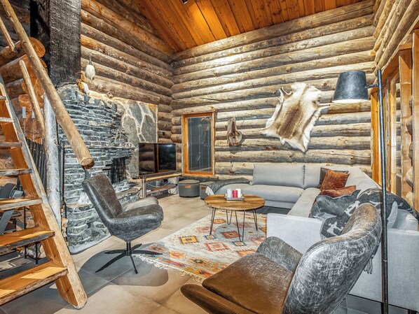 A log cabin interior with a stone fireplace, a sofa, a chair, and a hanging fur rug.