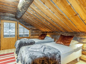 A log cabin bedroom with a sloped ceiling, two beds, a window, and a wooden door. - Kelohippu 2 by Interhome (Pelkosenniemi)