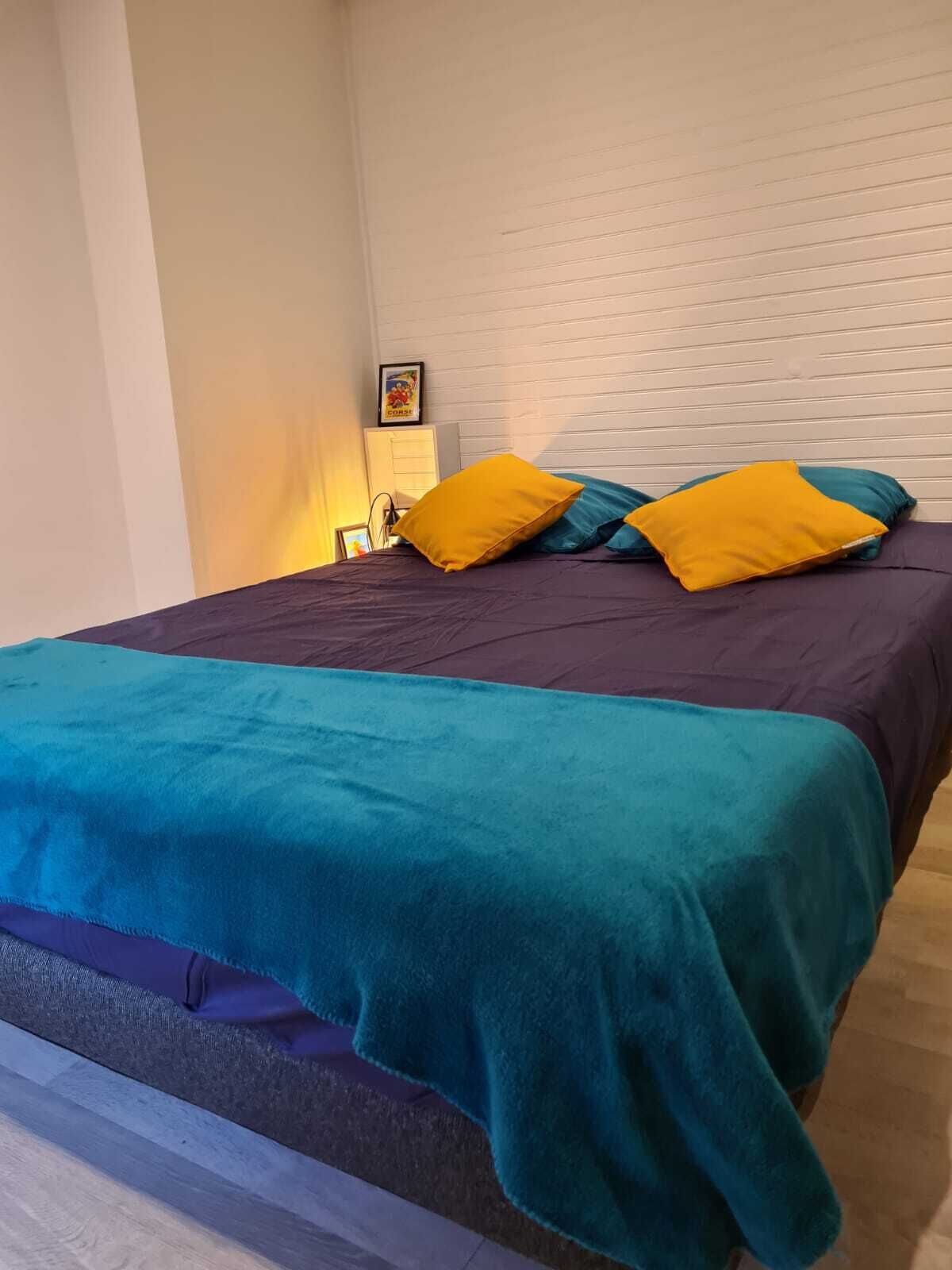 A bed with a teal and purple bedspread, two yellow pillows, and a teal blanket.