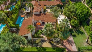 An aerial view of a resort with a swimming pool, palm trees, and a tiled-roof building.