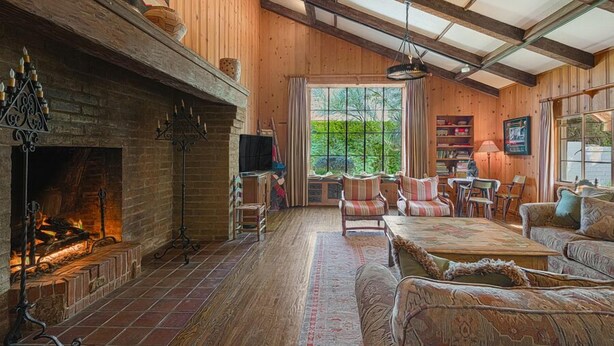 A cozy living room with a fireplace, wooden walls, and a large window.