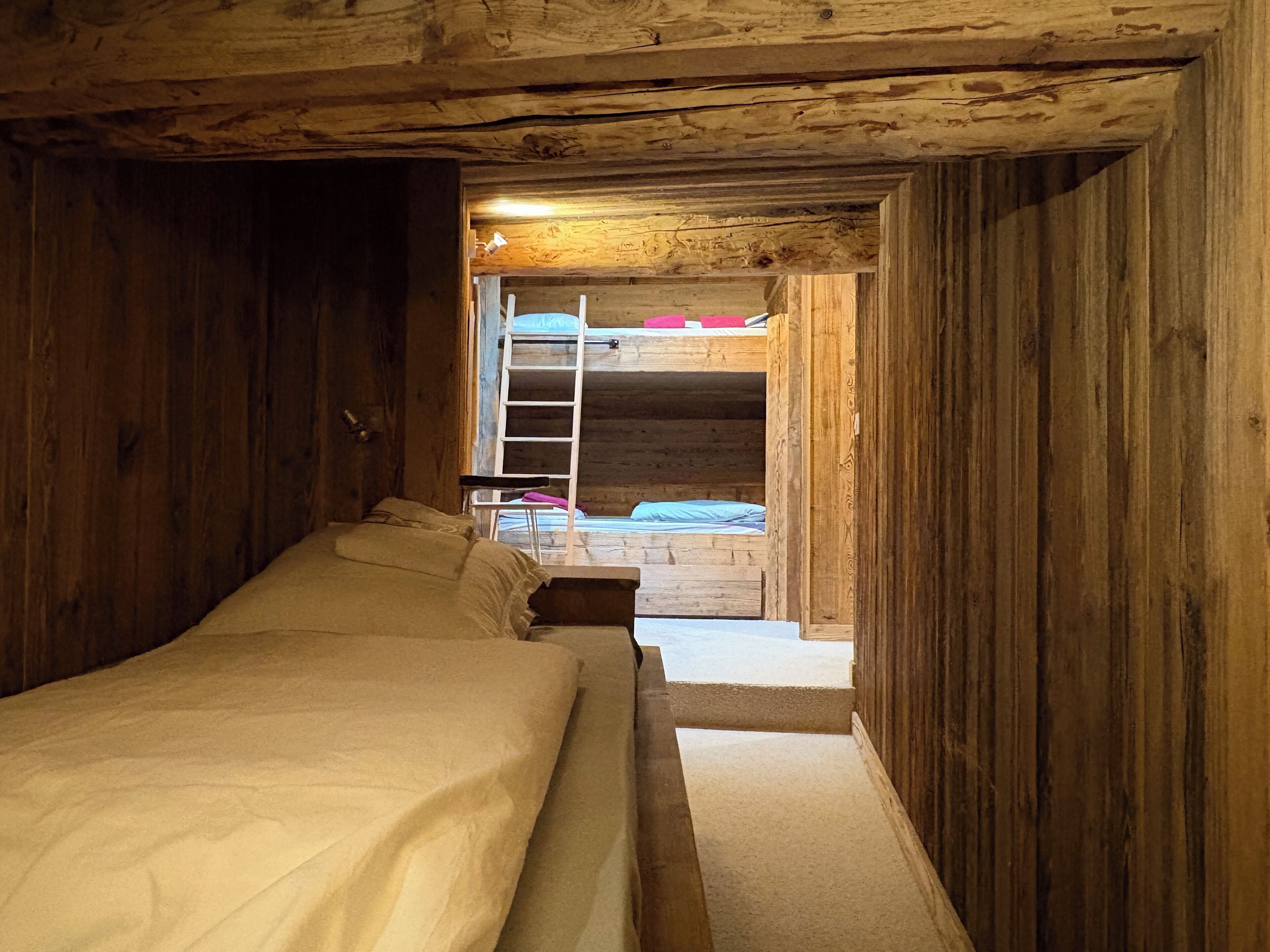 A wooden cabin room with a bunk bed and a ladder leading to an upper bunk.