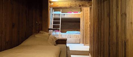 A wooden cabin room with a bunk bed and a ladder leading to an upper bunk.