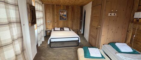 Una habitación con paneles de madera, dos camas, una mesita y un cuadro en la pared.