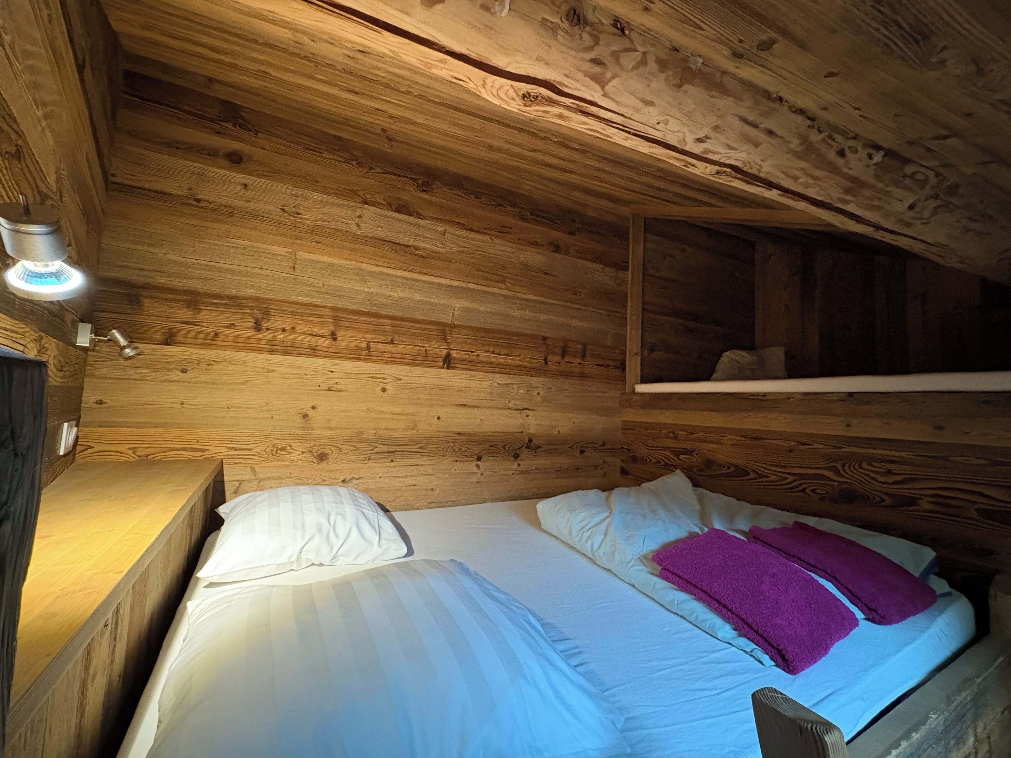 Une pièce de cabane en bois comprenant un lit, des oreillers, une table de chevet et une étagère.