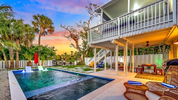 A pool area with a hot tub, lounge chairs, and a covered patio with outdoor furniture. - Anna Maria Gem! Pool, Canal Views and Style! (Anna Maria)