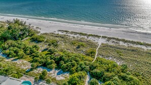 An aerial view of a beach with a clear sky, a sandy shore, and dense vegetation in the foreground. - Anna Maria Gem! Pool, Canal Views and Style! (Anna Maria)