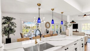 A modern kitchen with a central island, white cabinetry, and blue pendant lights. - Anna Maria Gem! Pool, Canal Views and Style! (Anna Maria)