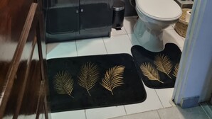 Une petite salle de bain avec un lavabo blanc, des meubles noirs, des toilettes et une poubelle. On trouve deux tapis noirs ornés de motifs dorés sur le sol.