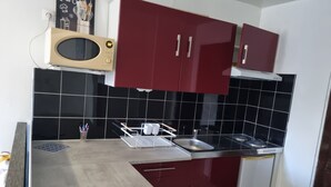 Une cuisine avec des meubles de rangement rouges, un four à micro-ondes, un évier et un dosseret carrelé.