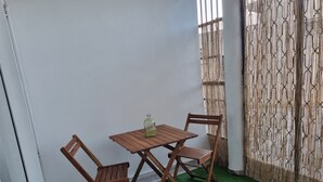 Un petit espace extérieur aménagé avec une table en bois et deux chaises, une bouteille posée sur la table et un paravent en bambou en arrière-plan.