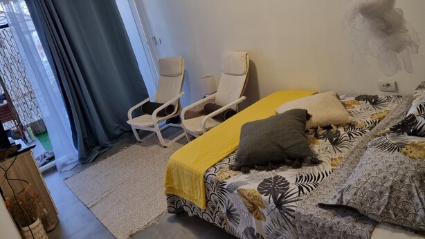Une chambre à coucher avec un lit, deux chaises, un rideau, une horloge murale et un petit tapis.