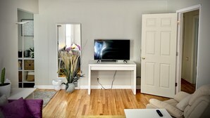A living room with a TV on a white stand, a door, a bookshelf, and a purple couch. - Spacious Home 8 min to ND and Memorial Hospital (South Bend)