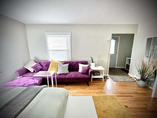 Un salon moderne avec un canapé violet, une table basse blanche et une petite table d’appoint blanche agrémentée d’une plante.