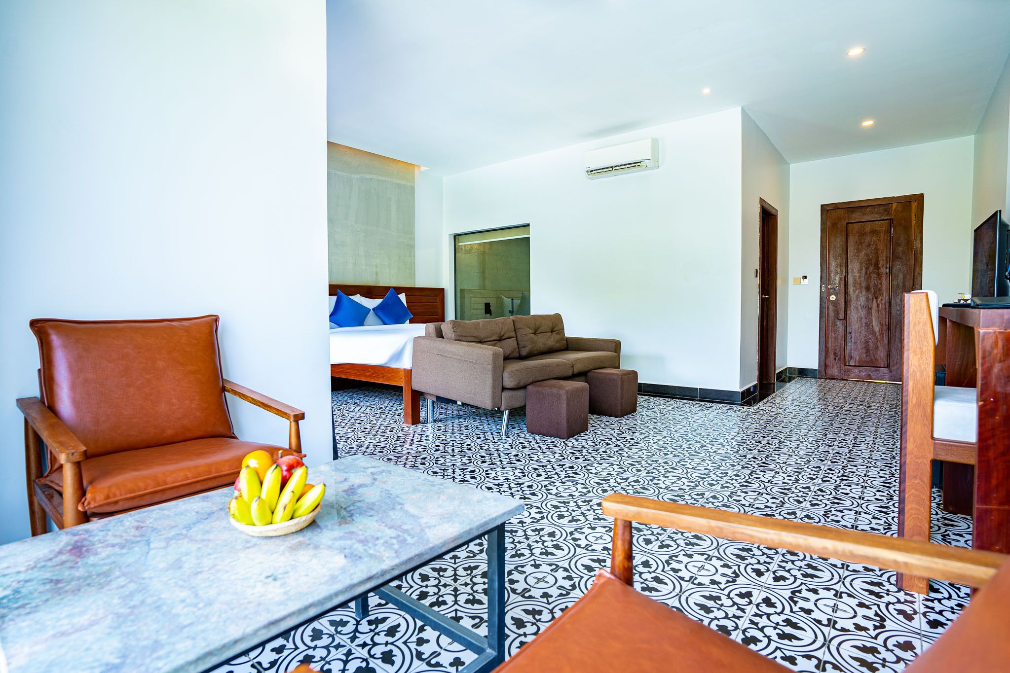 A hotel room with a sofa, armchair, and a table with fruit.