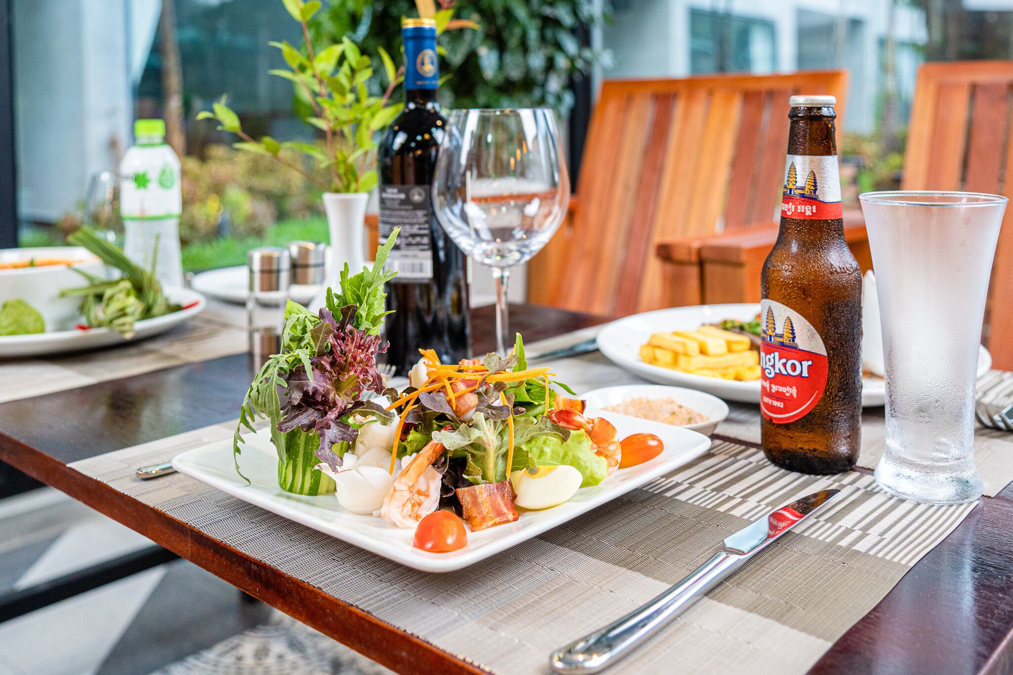 A dining table with a plate of food, a bottle of beer, a glass of water, and a wine glass.