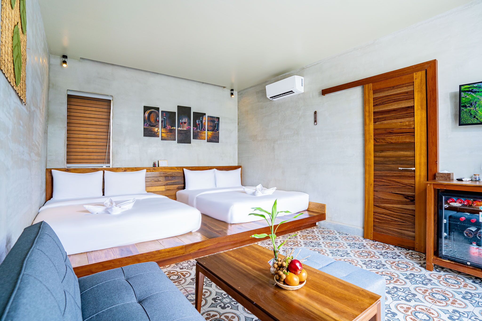 Una habitación de hotel moderna con una cama grande, dos sofás blancos, una mesa de centro de madera con fruta y un suelo estampado.