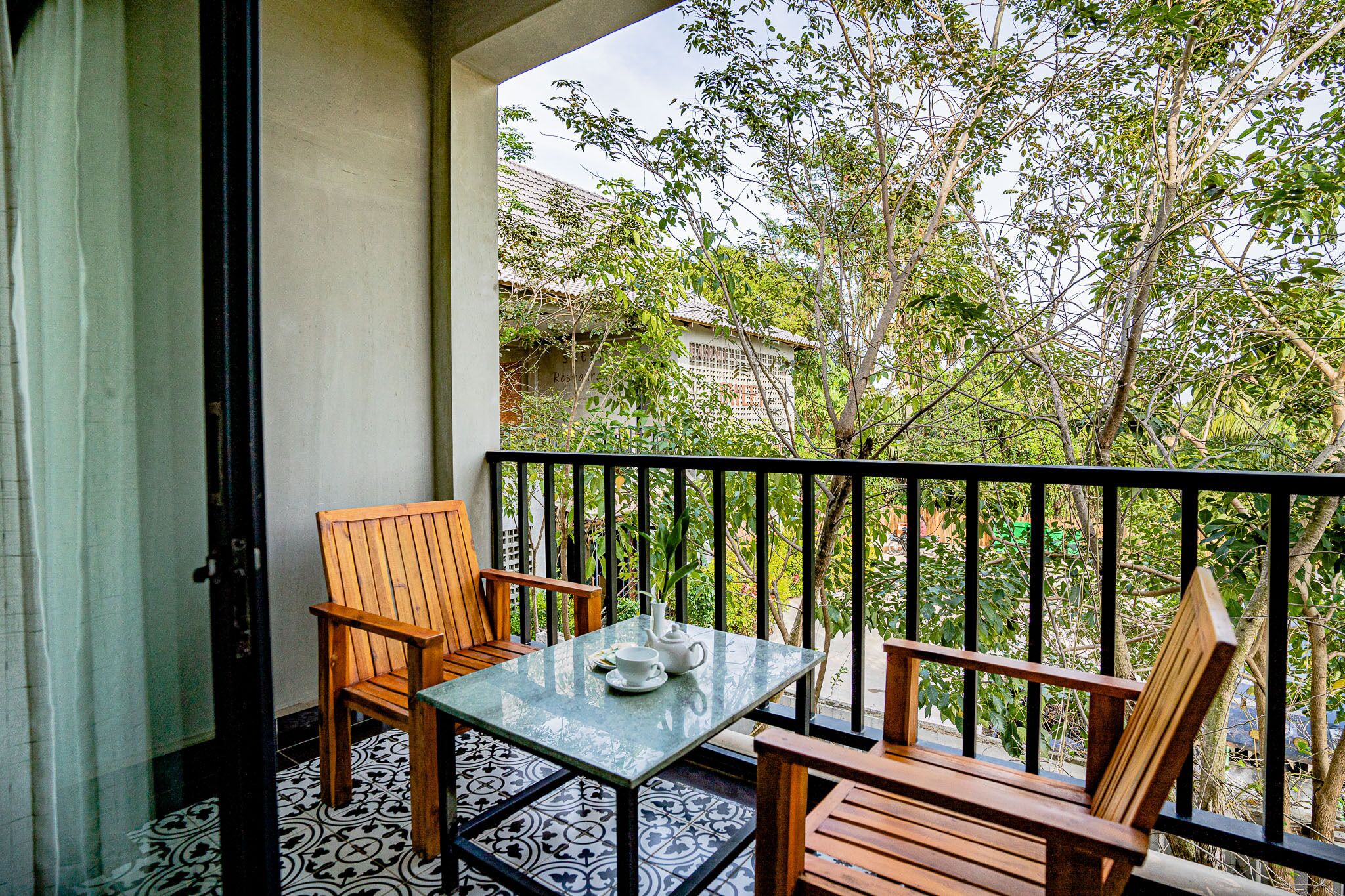 A balcony with a table and chairs, a view of trees and buildings, and a patterned floor.
