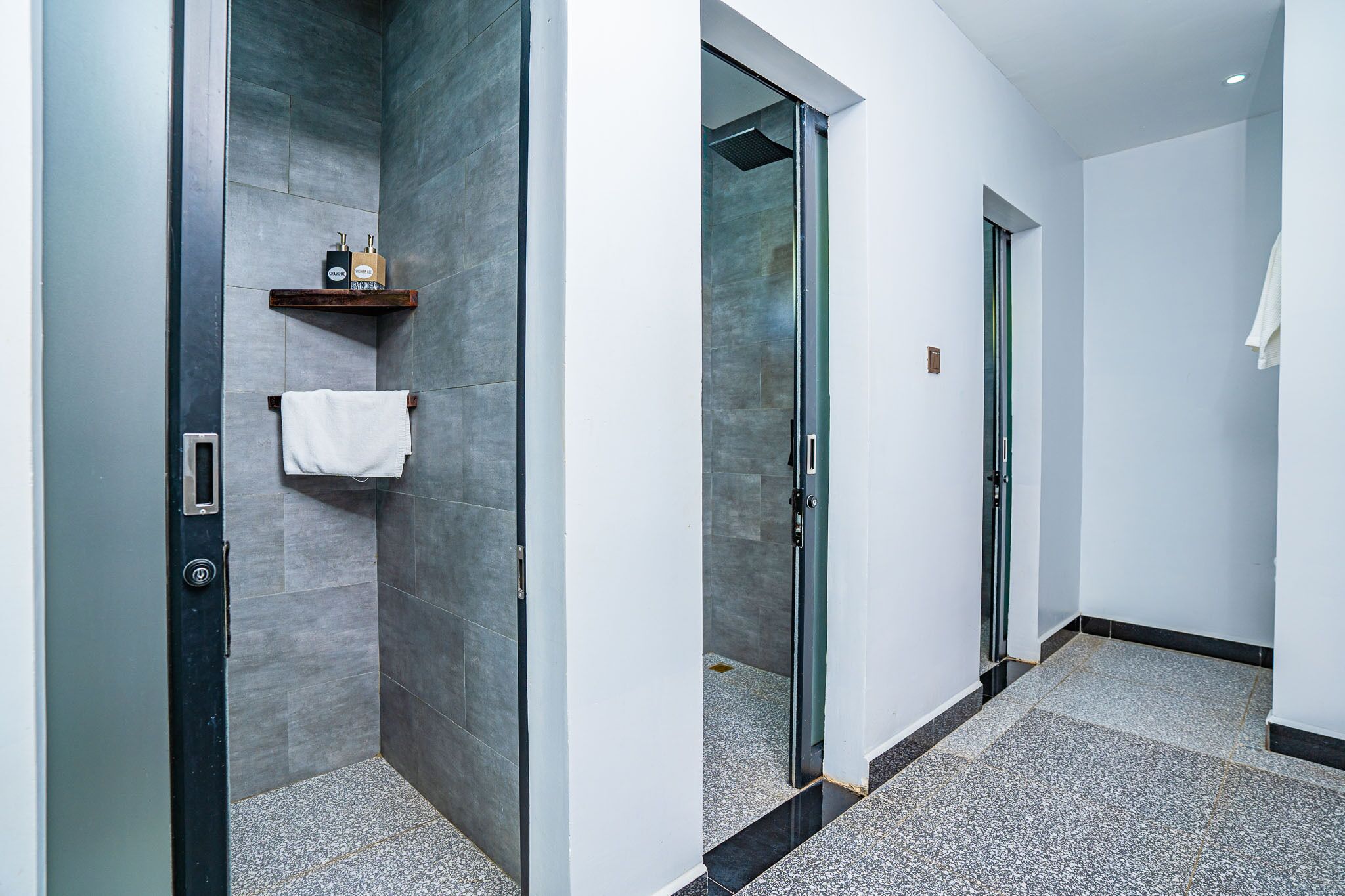 A modern bathroom with a glass shower enclosure, a white towel hanging on the wall, and a small shelf with toiletries.