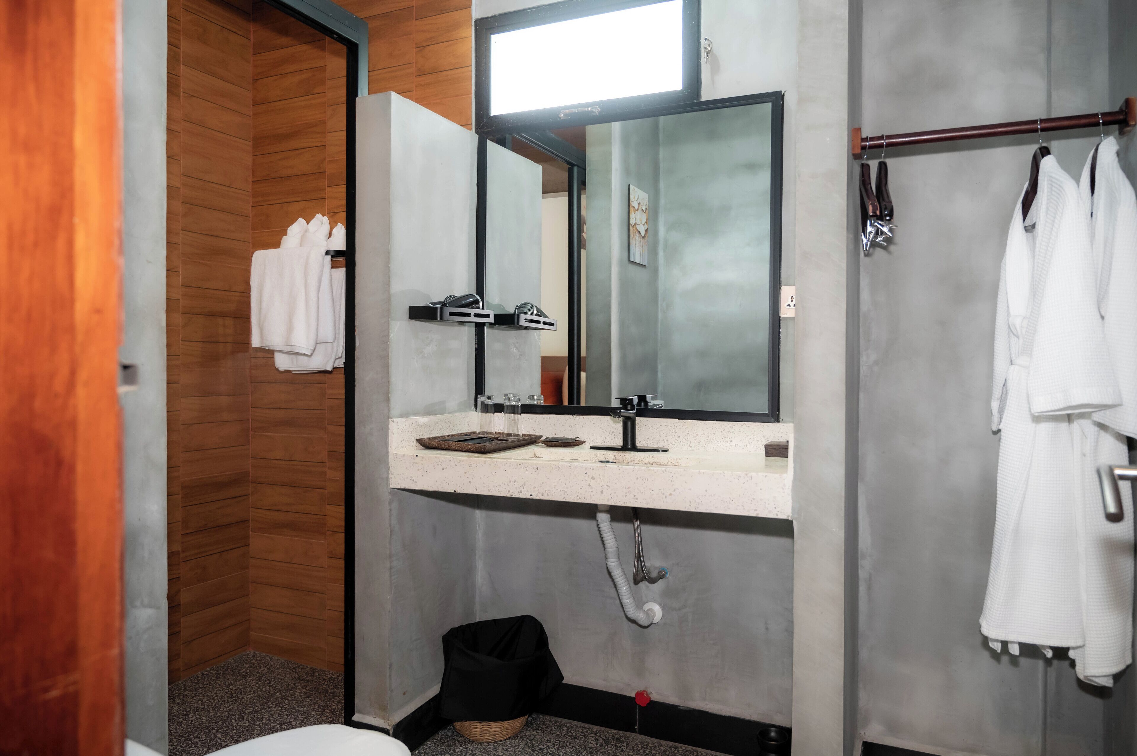 A modern bathroom with a wooden wall, a large mirror, a white sink, and a towel rack.
