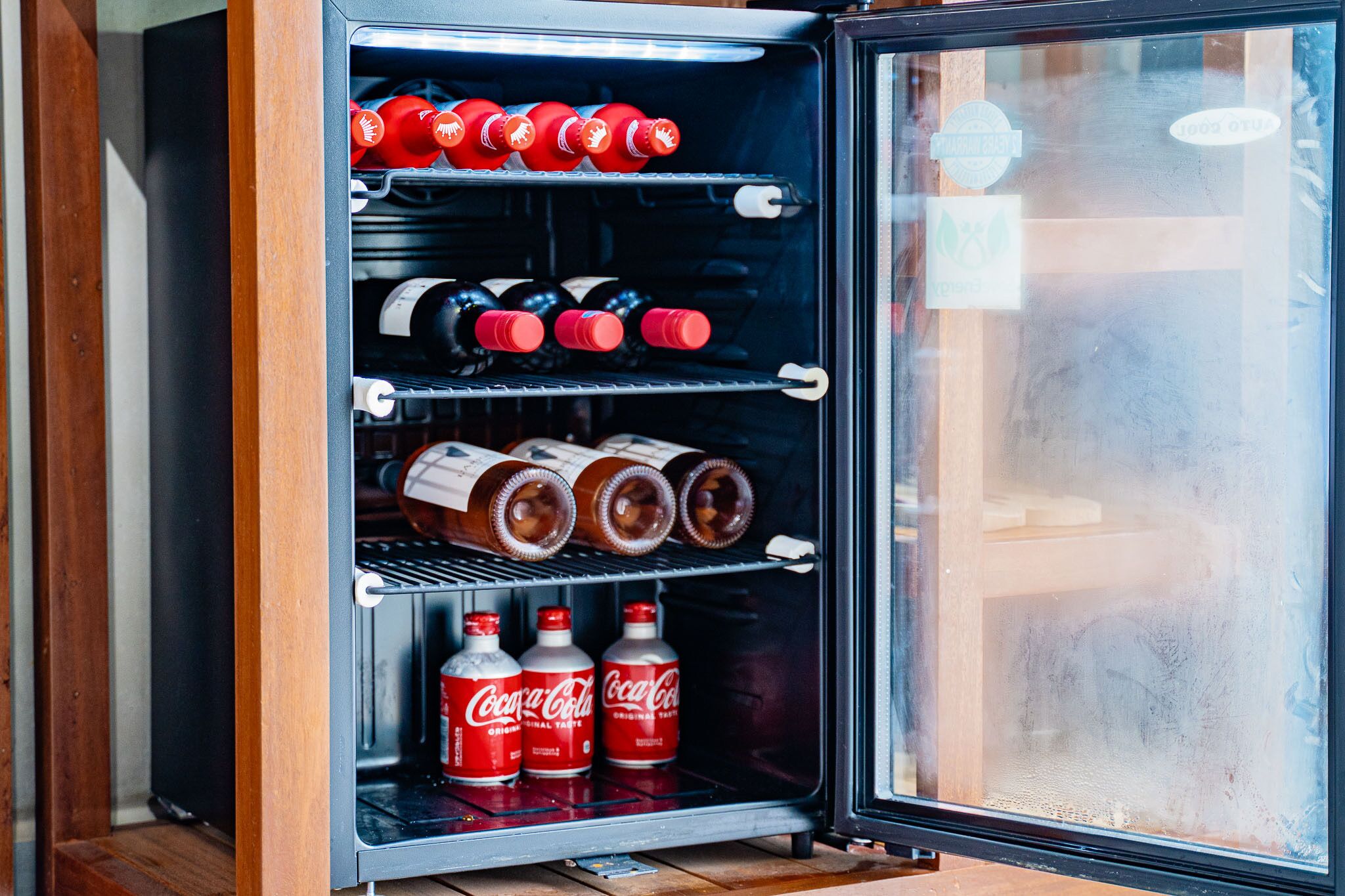 Un petit réfrigérateur rempli de diverses boissons, notamment des bouteilles de Coca-Cola et des bouteilles de vin.