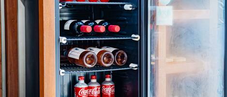 Un petit réfrigérateur rempli de diverses boissons, notamment des bouteilles de Coca-Cola et des bouteilles de vin.