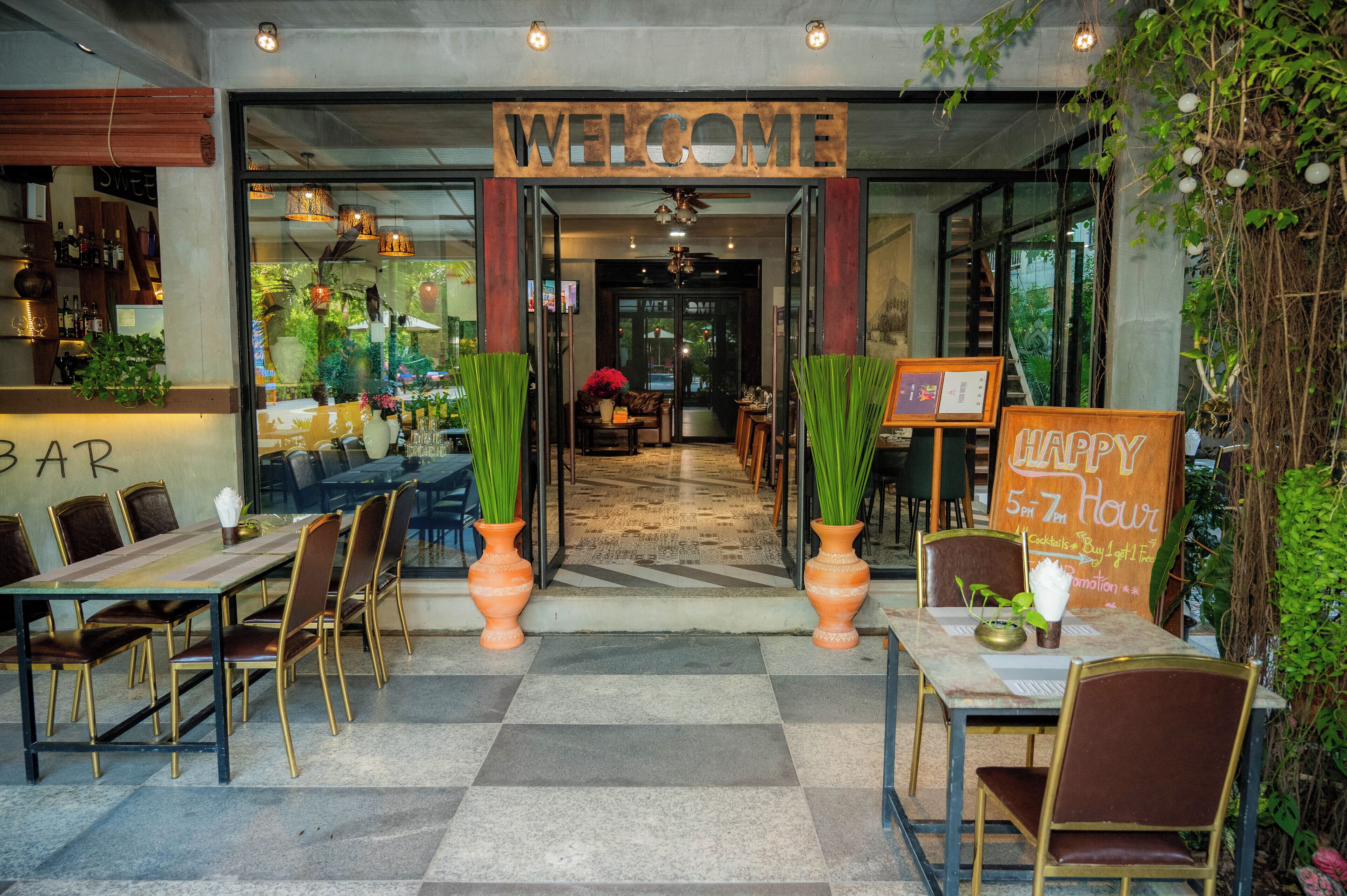 A restaurant entrance with a 'WELCOME' sign, outdoor seating with tables and chairs, and a 'HAPPY 5 PM ZEN Hour' sign.