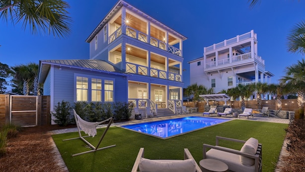 Une maison à deux étages avec une piscine, un espace salon extérieur et une pelouse bien entretenue.