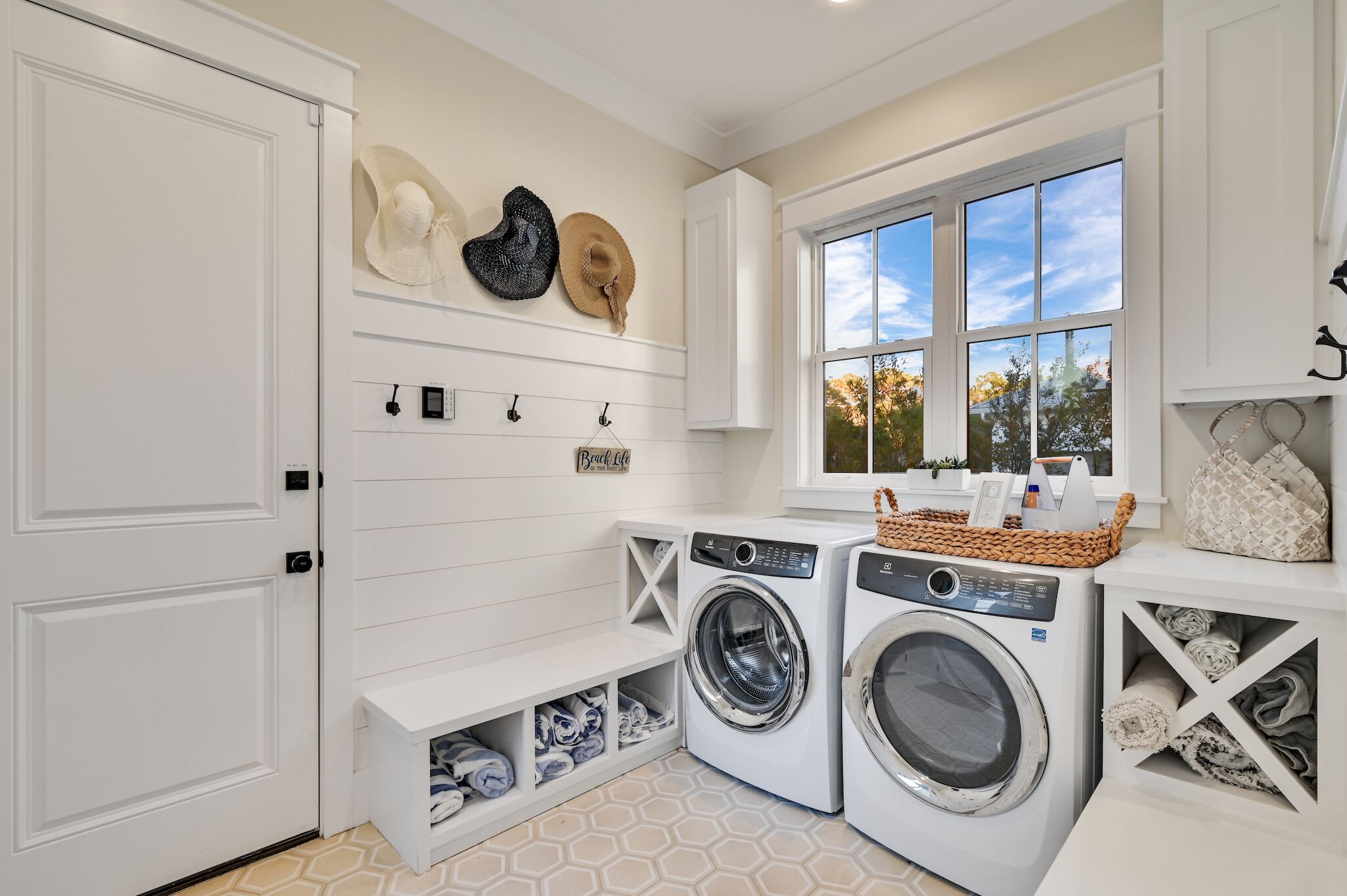 A laundry room with two front-loading washing machines, a drying rack, and a shelf with neatly folded towels.