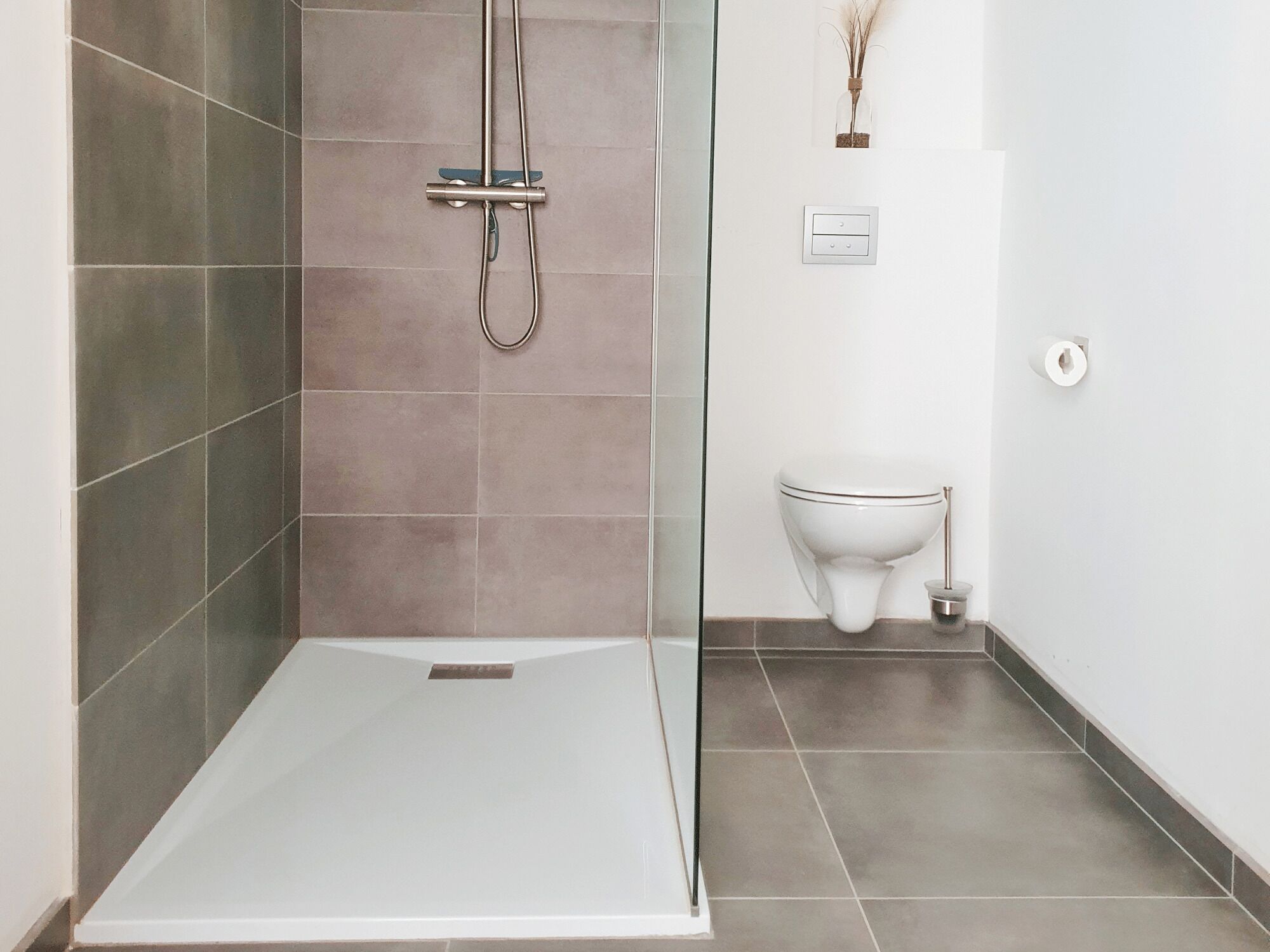 A modern bathroom with a shower, toilet, and a small shelf with decorative items.