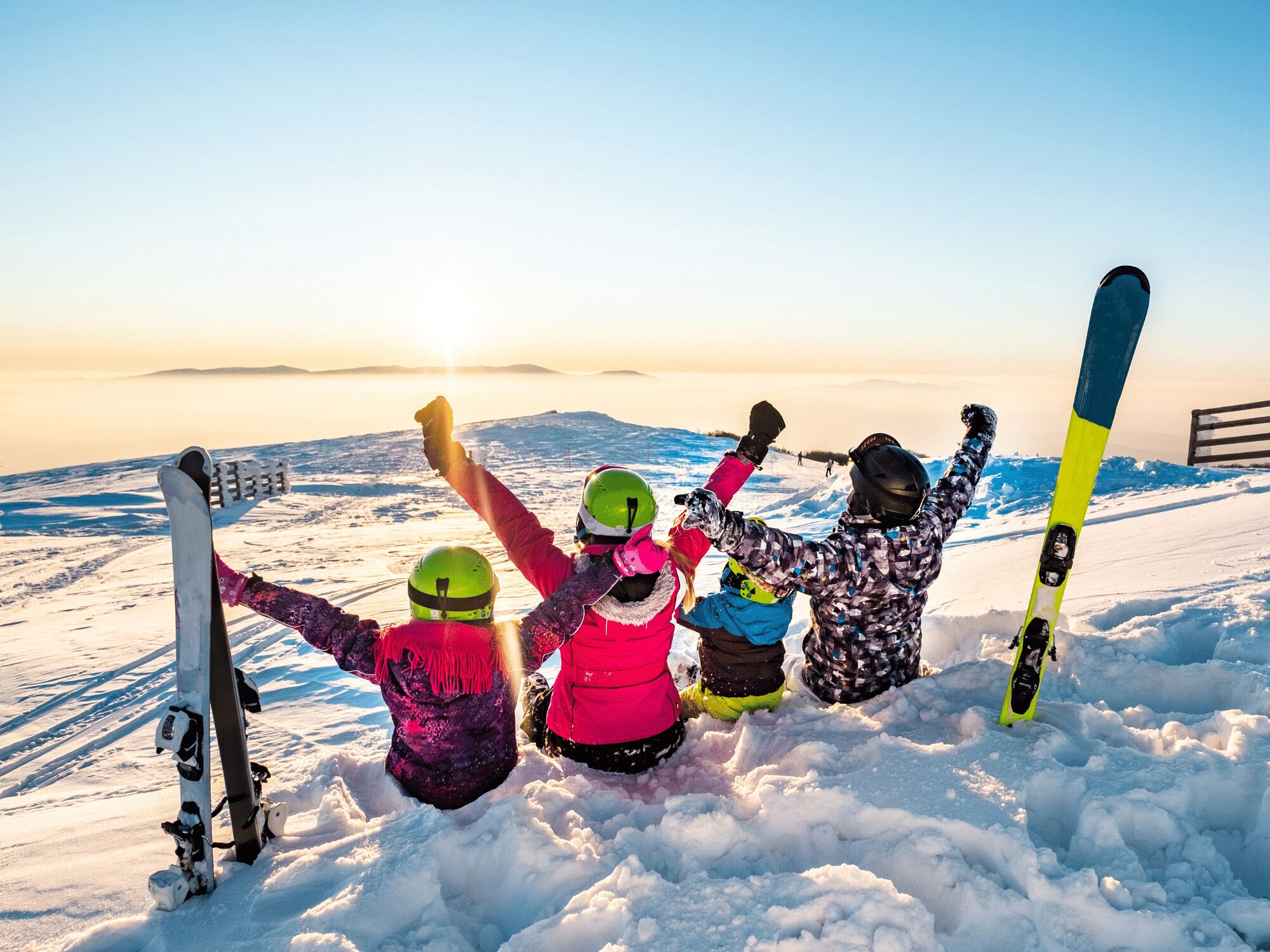 A group of people on a snowy mountain with skis, celebrating at sunset.
