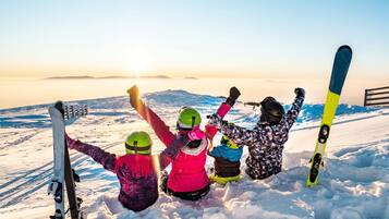 A group of people on a snowy mountain with skis, celebrating at sunset.