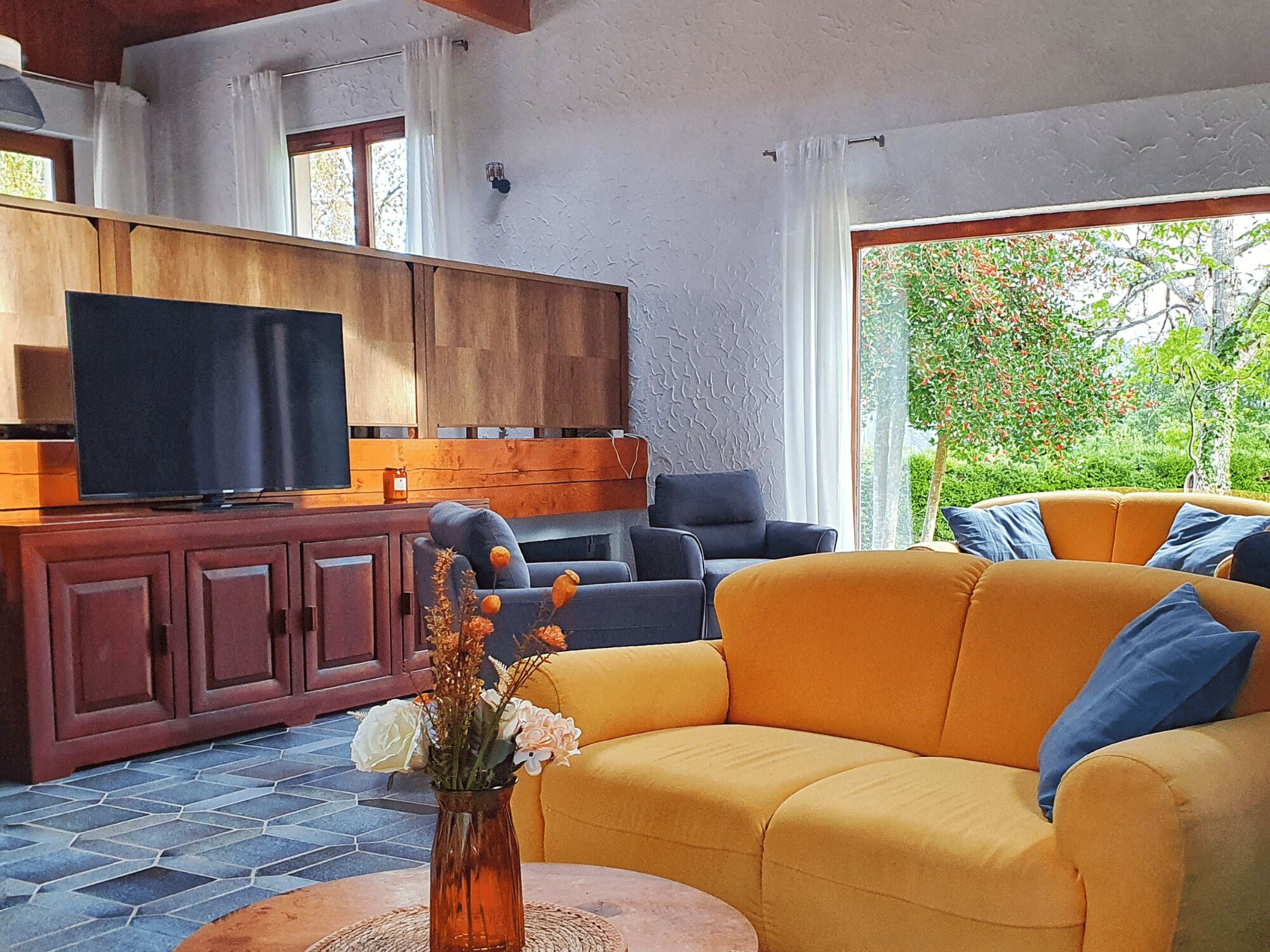 A living room with a yellow sofa, a dark blue sofa, a wooden cabinet, and a television.