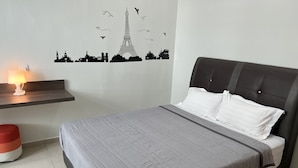 Una cama bien hecha con colcha gris y almohadas blancas, una mesita de noche con lámpara y un adhesivo mural con monumentos parisinos.
