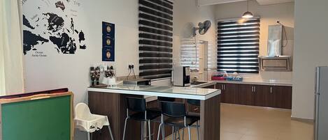 Uma cozinha moderna com uma ilha central, banquetas, geladeira e um espaço de refeições com um quadro negro verde.