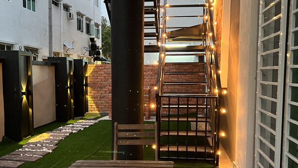 Un patio con mesa y banco de madera, rodeado por un muro de ladrillo y un edificio blanco.