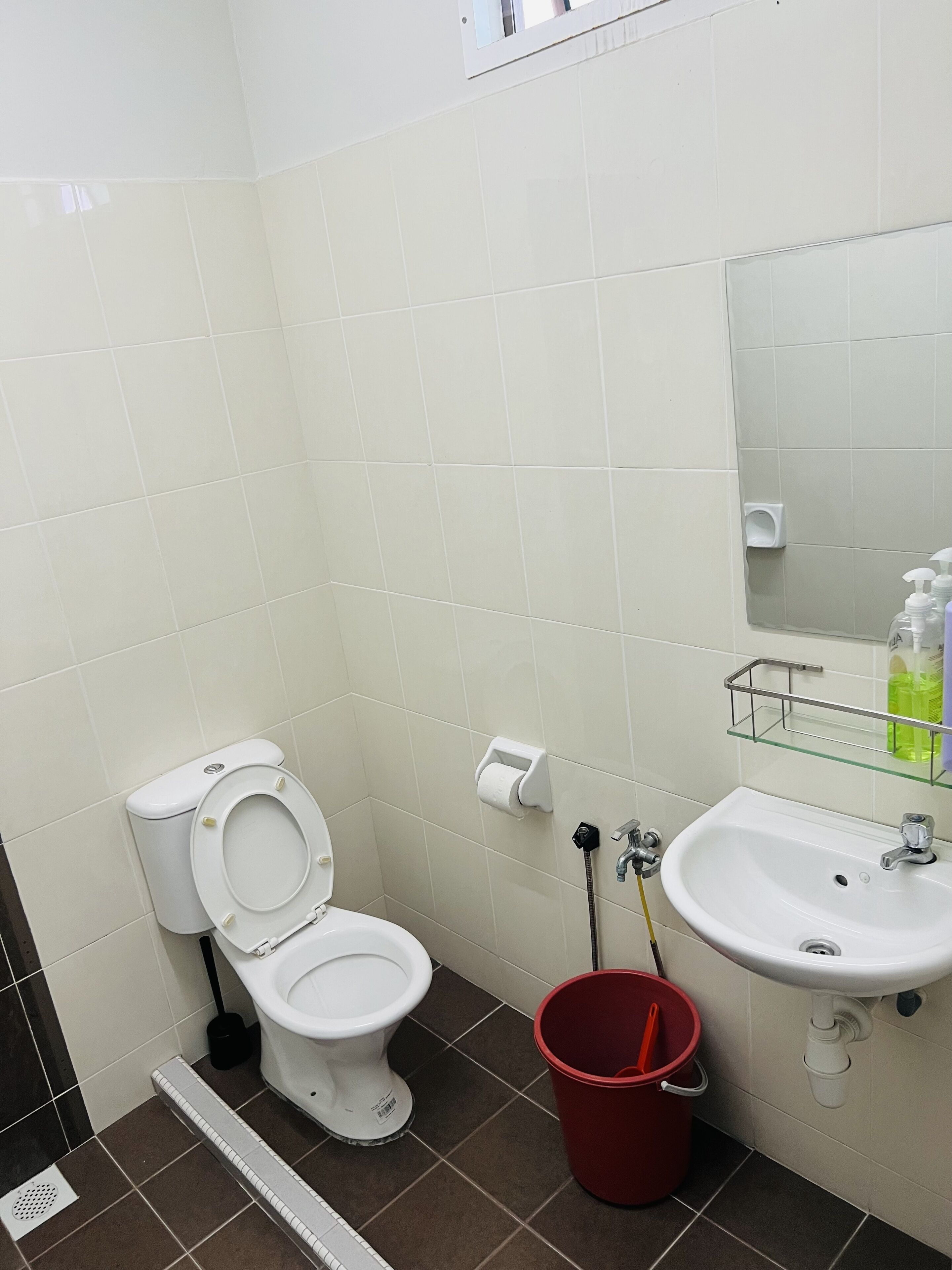 A bathroom with a toilet, sink, and a red bucket.