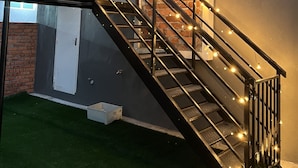 Una escalera moderna con barandilla de metal y luces de cuerda, que conduce a un muro de ladrillo y una puerta.