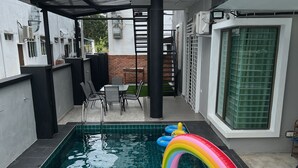 Una piscina en la azotea con un tobogán hinchable de arcoíris, rodeada por un porche cubierto con sillas y una mesa.