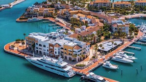 An aerial view of a coastal resort with multiple buildings, a marina with yachts, and clear blue waters.