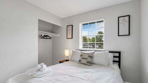 Una camera da letto con un letto, una finestra, un comodino e una mensola fissata al muro.