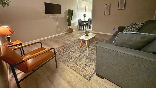Un soggiorno con un divano, un tavolo, una sedia, una TV a parete e una pianta in vaso.