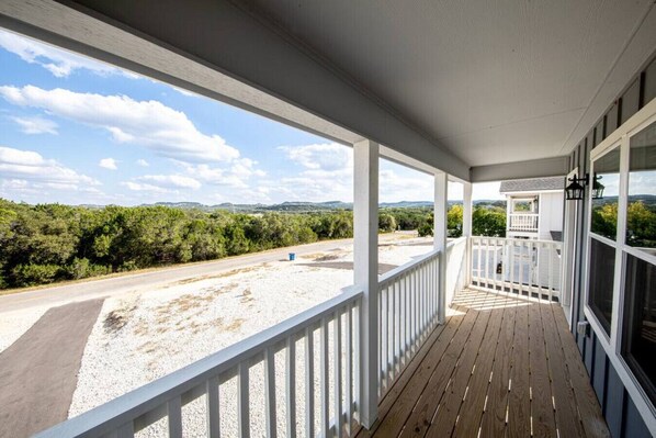 A covered porch with a view of a road and greenery.
