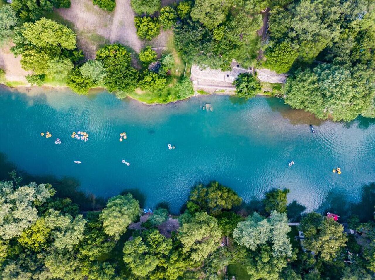 Vista aérea de un lago rodeado de bosque denso, con varias embarcaciones ancladas cerca de la orilla.