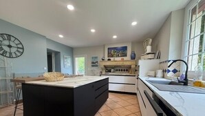 Una cocina moderna con una isla central, armarios blancos y un amplio ventanal que proporciona luz natural.