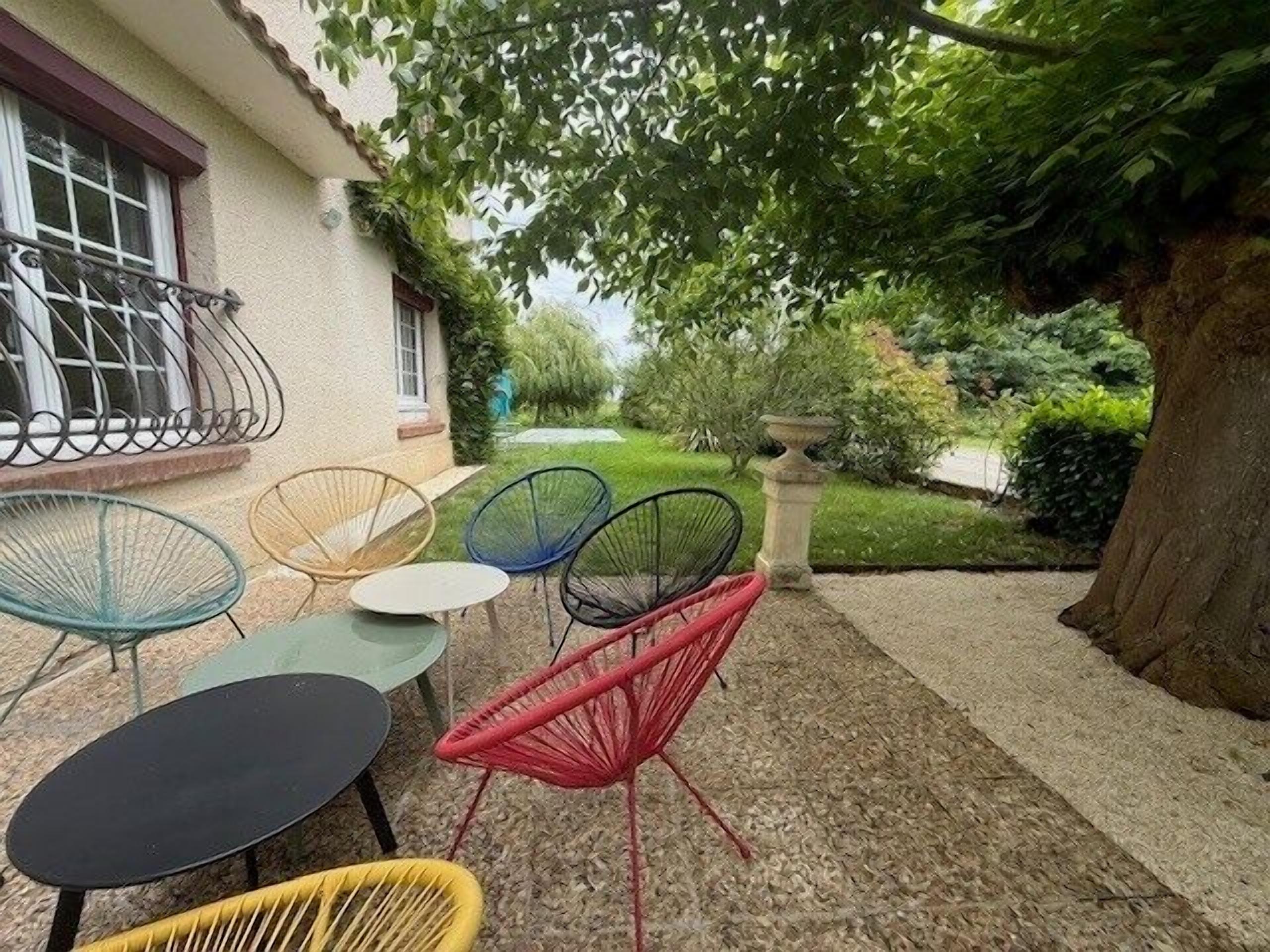 Un espace extérieur aménagé avec plusieurs chaises et tables, un chemin en pierre et un grand arbre.